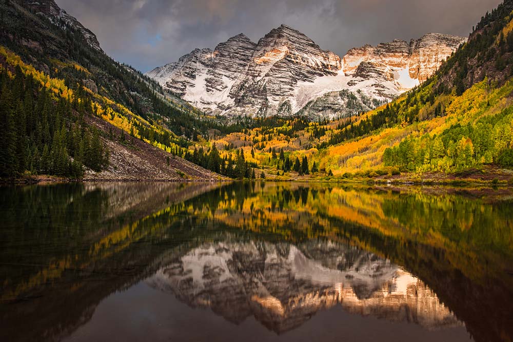 Colorado - lake with surrounding mountains covered with trees. In the background is a snow-covered mountain.