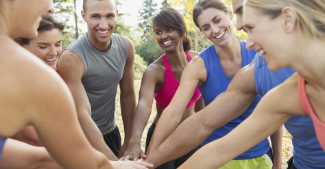 A team of people dressed in fitness clothes joining hands in the middle of a circle and enjoying themselves