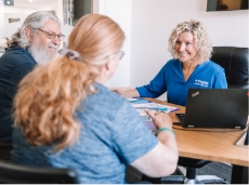 A couple sits at a desk while talking to an insurance agent.