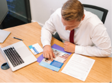 A man wearing a shirt and tie looks down at a Fidelis flyer while working at an office desk.